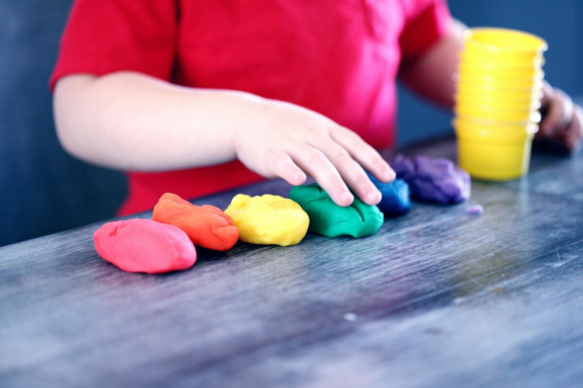 La mano di un bambino modella pezzi di plastilina colorata su un tavolo